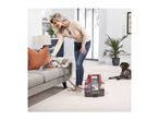 Woman cleaning a grey sofa with a Vax SpotWash carpet cleaner, with a dog nearby.