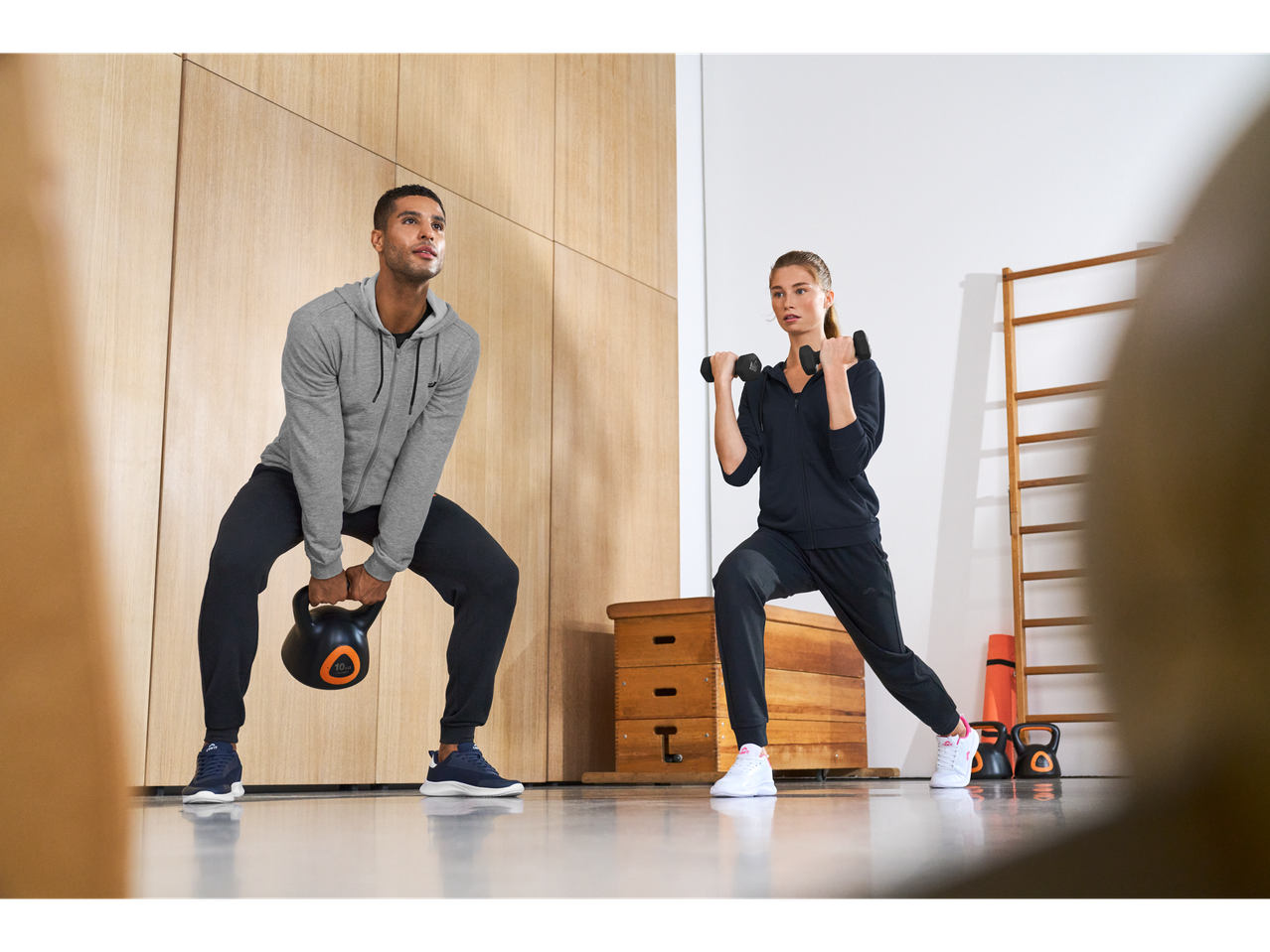 Homem com kettlebell e mulher com halteres, ambos a usar sapatilhas desportivas Crivit.