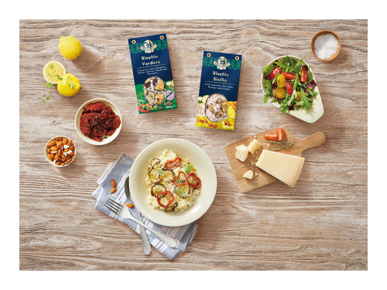 Two risotto mixes, one with vegetables and one with almonds, zucchini, orange, and lemon, on a wooden table with ingredients and a prepared dish.