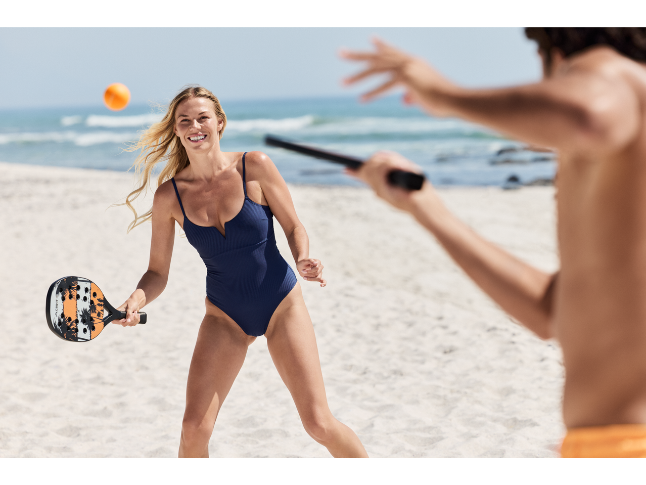 Femeie în costum de baie CRIVIT jucând tenis de plajă pe nisip.
