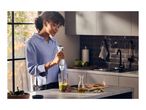 A woman uses a hand blender to mix ingredients in a kitchen.