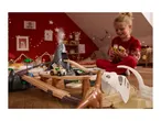 A child plays with a dinosaur-themed wooden train set and toy cars in a festive room.
