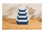 Stack of four collapsible blue food storage containers with white lids on a wooden table.