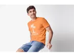 Muški model u narančastoj majici s printom palmi i trapericama.