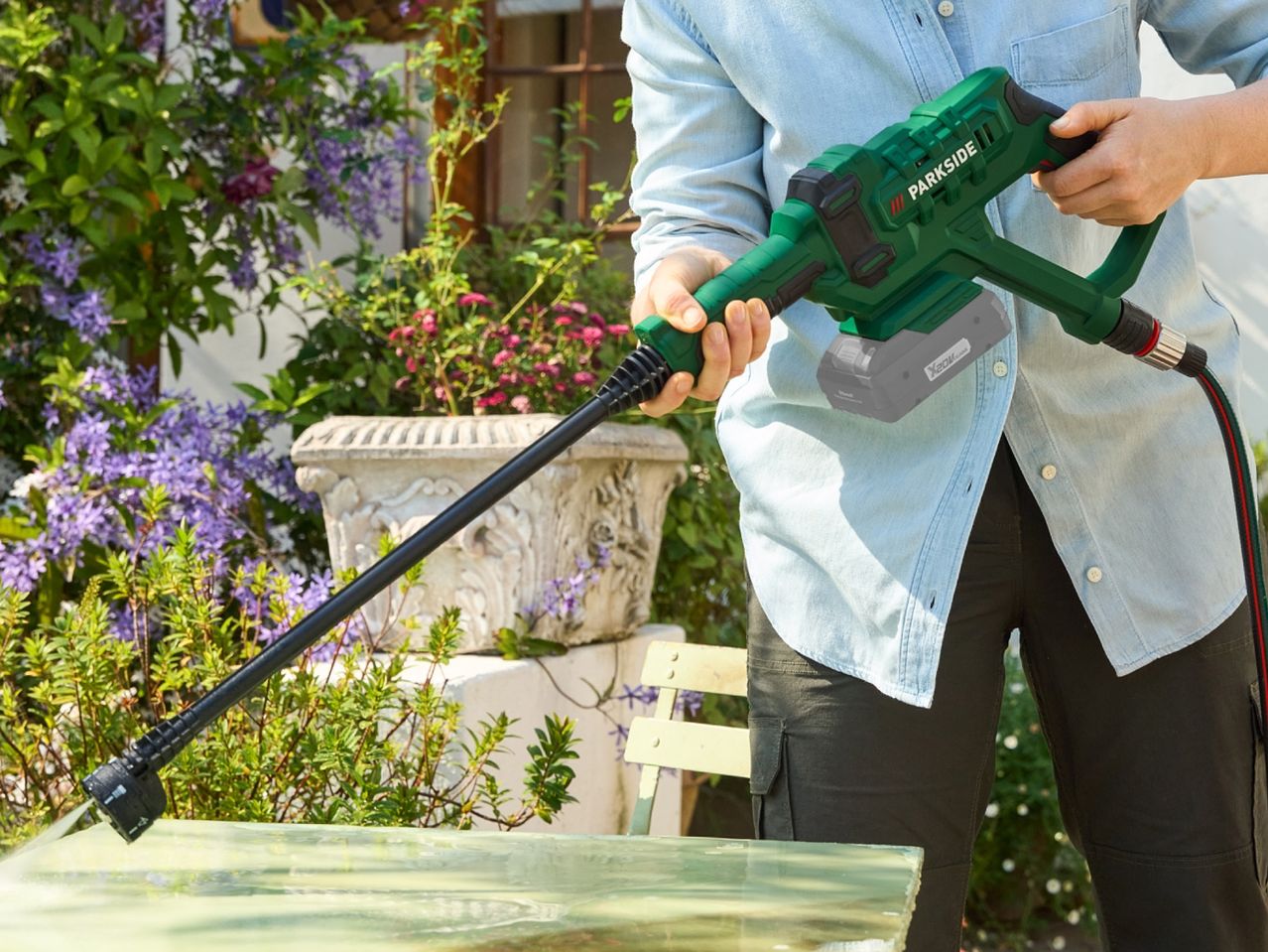 A person uses a Bosch pressure washer to clean a patio table.