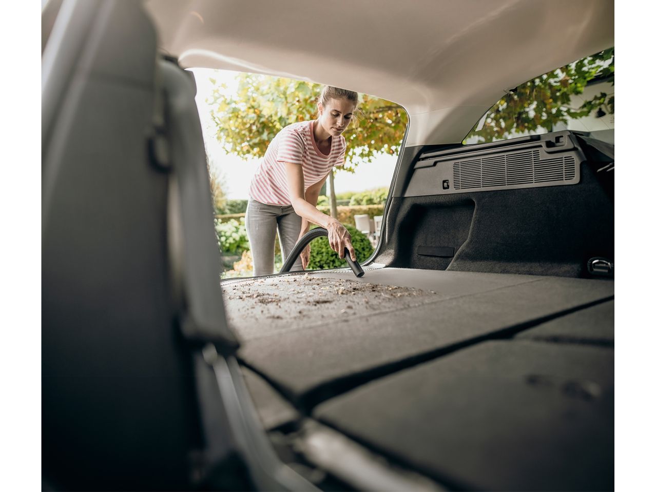 Una donna pulisce il bagagliaio della sua auto con un aspirapolvere.
