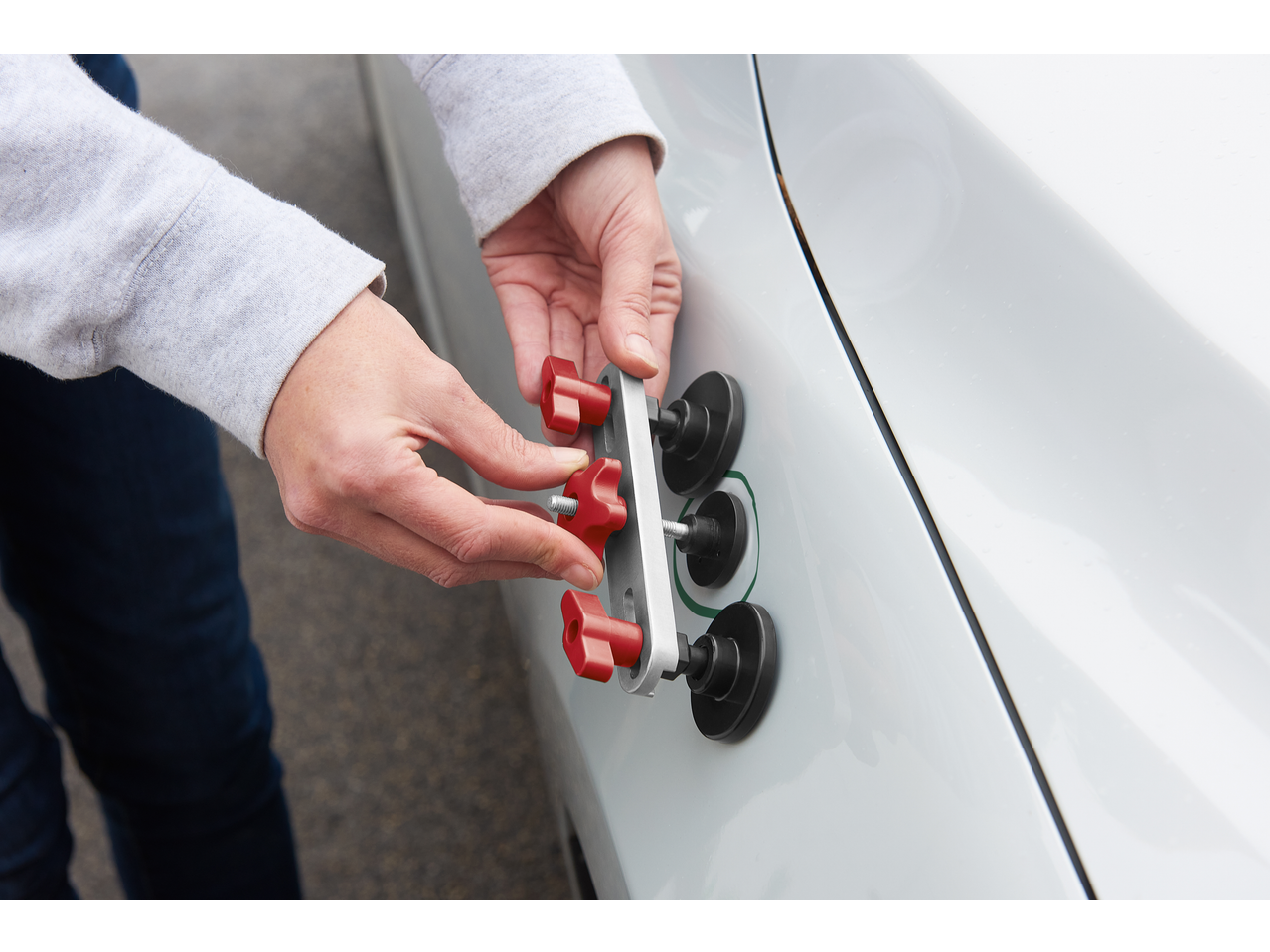 Hands using a Parkside® Dent Repair Kit on a white car.