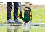 A person using a submersible pump to drain water from a pond in a garden.