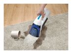 Handheld spot cleaner removing a spill from a shaggy rug next to a wooden floor.