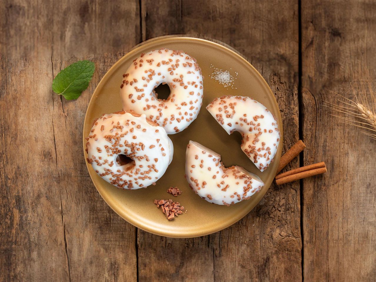 Fehér mázas fánkok csokoládédarabkákkal egy arany tányéron, mentával és fahéjjal.