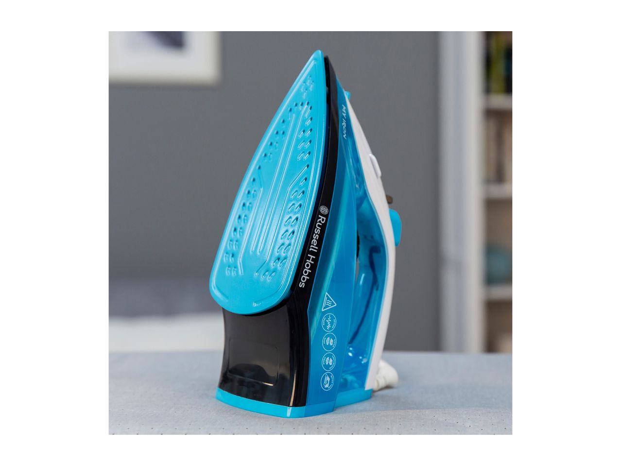 A blue and black Russell Hobbs iron standing upright on an ironing board.
