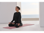 Woman meditating on a yoga mat, wearing a black sweatshirt and trousers.
