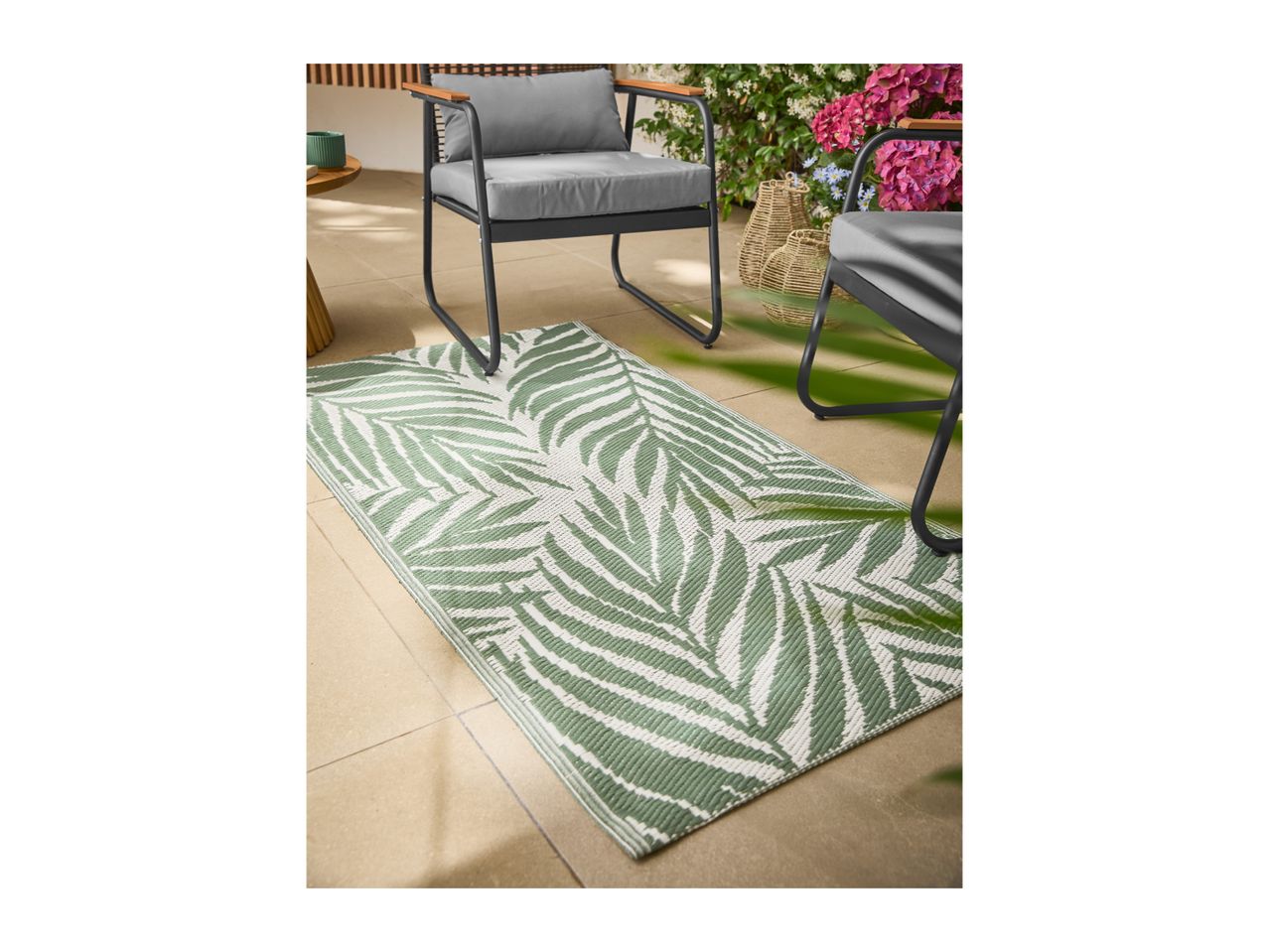 Outdoor rug with green palm leaf pattern on a patio with garden chairs and plants.