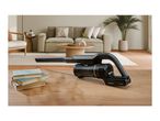 A black handheld vacuum cleaner on a wooden table next to a stack of books.