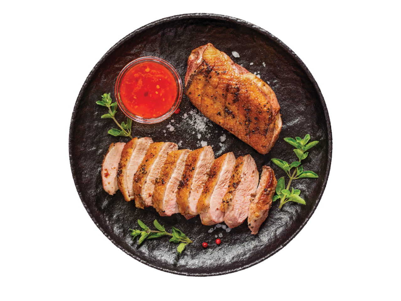 Cepta pīles krūtiņa ar sarkanu mērci un zaļumiem uz melna šķīvja.