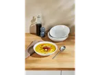 Un bol cu supă cremoasă este servit alături de boluri stivuite pe o masă din lemn.