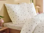 White bedding with small floral and strawberry patterns on a bed with a wooden frame.