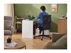 Man working on a laptop at a white desk in a home office with green walls.