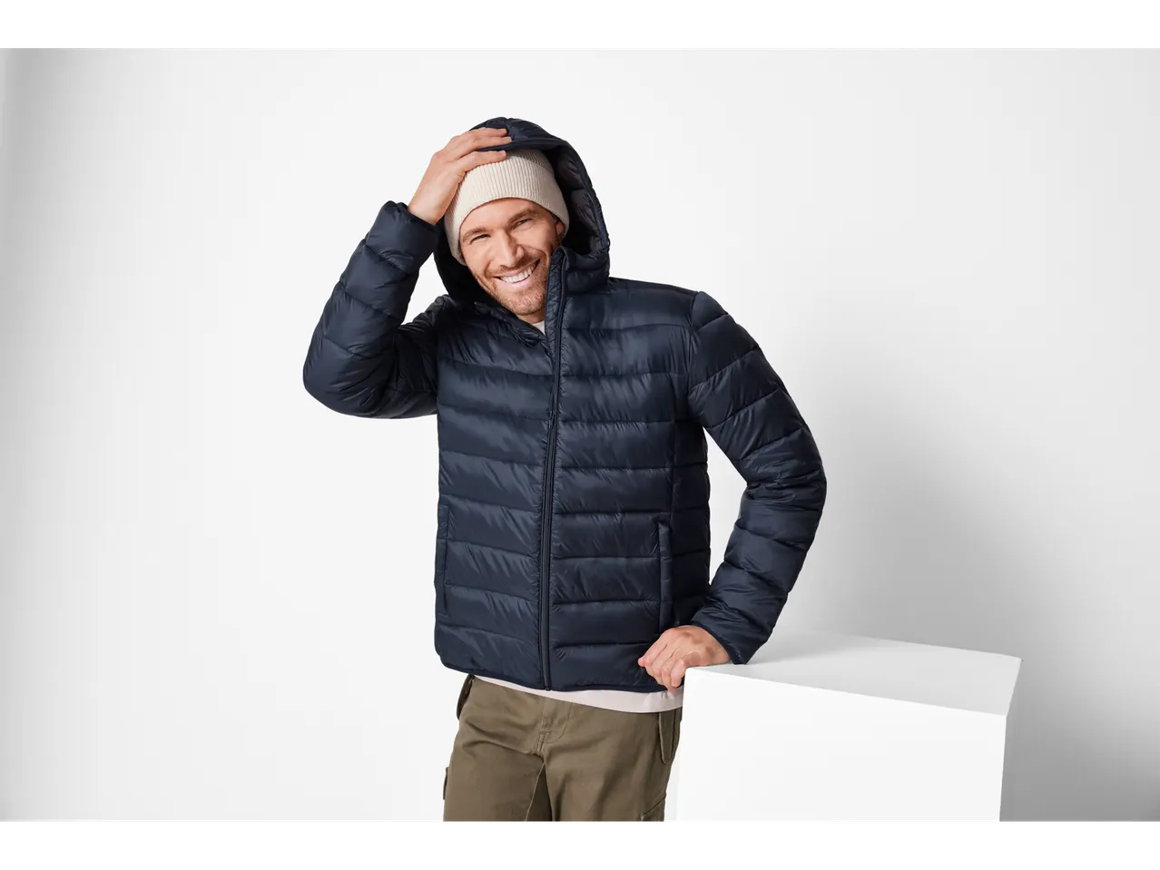 Uomo sorridente con giacca leggera blu navy e berretto beige.