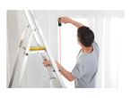 Man on a ladder using a laser distance meter to measure a window frame.