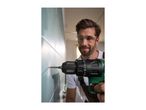 Man drilling into a tiled wall with a cordless drill, wearing safety glasses.