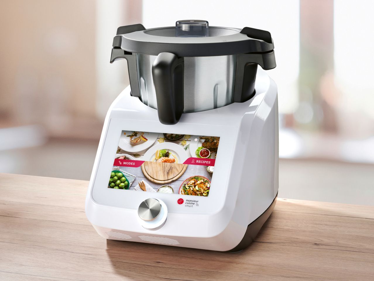 A white and black Monsieur Cuisine Smart food processor with a digital screen displaying recipes.
