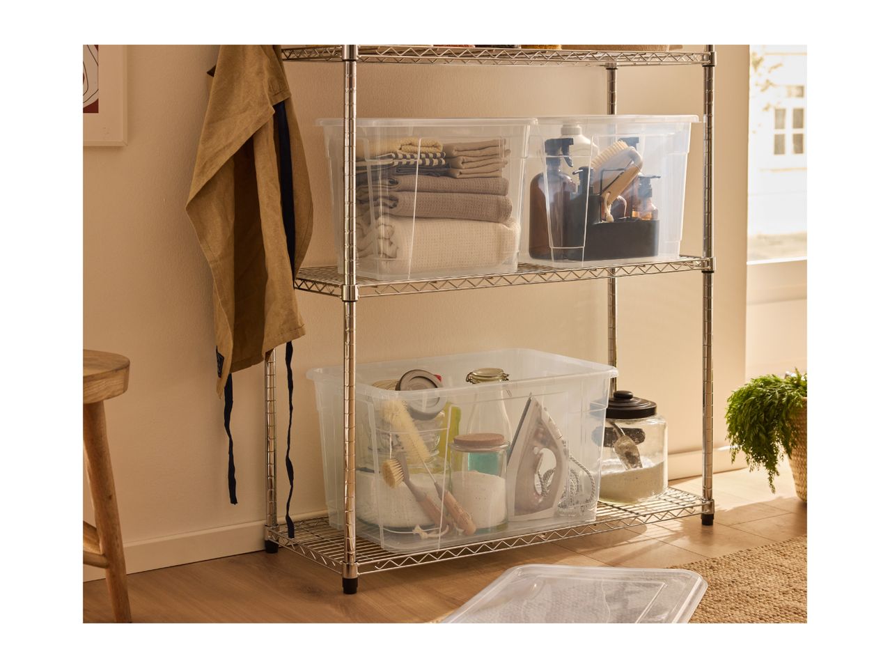 Chrome shelving unit with clear storage boxes holding towels, cleaning supplies, and laundry items.