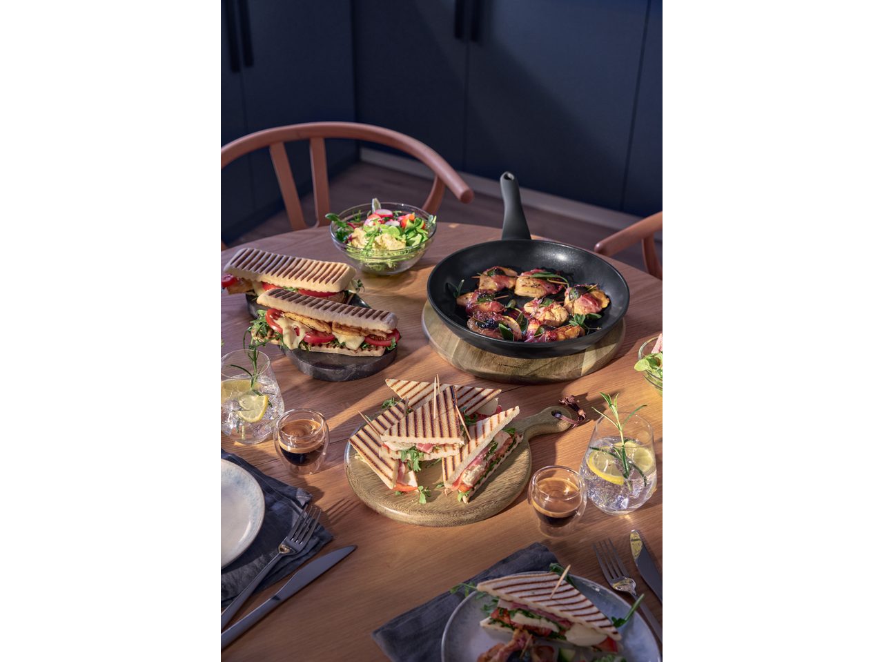 Table with paninis, grilled sandwiches, a frying pan with skewers, and a fresh salad.
