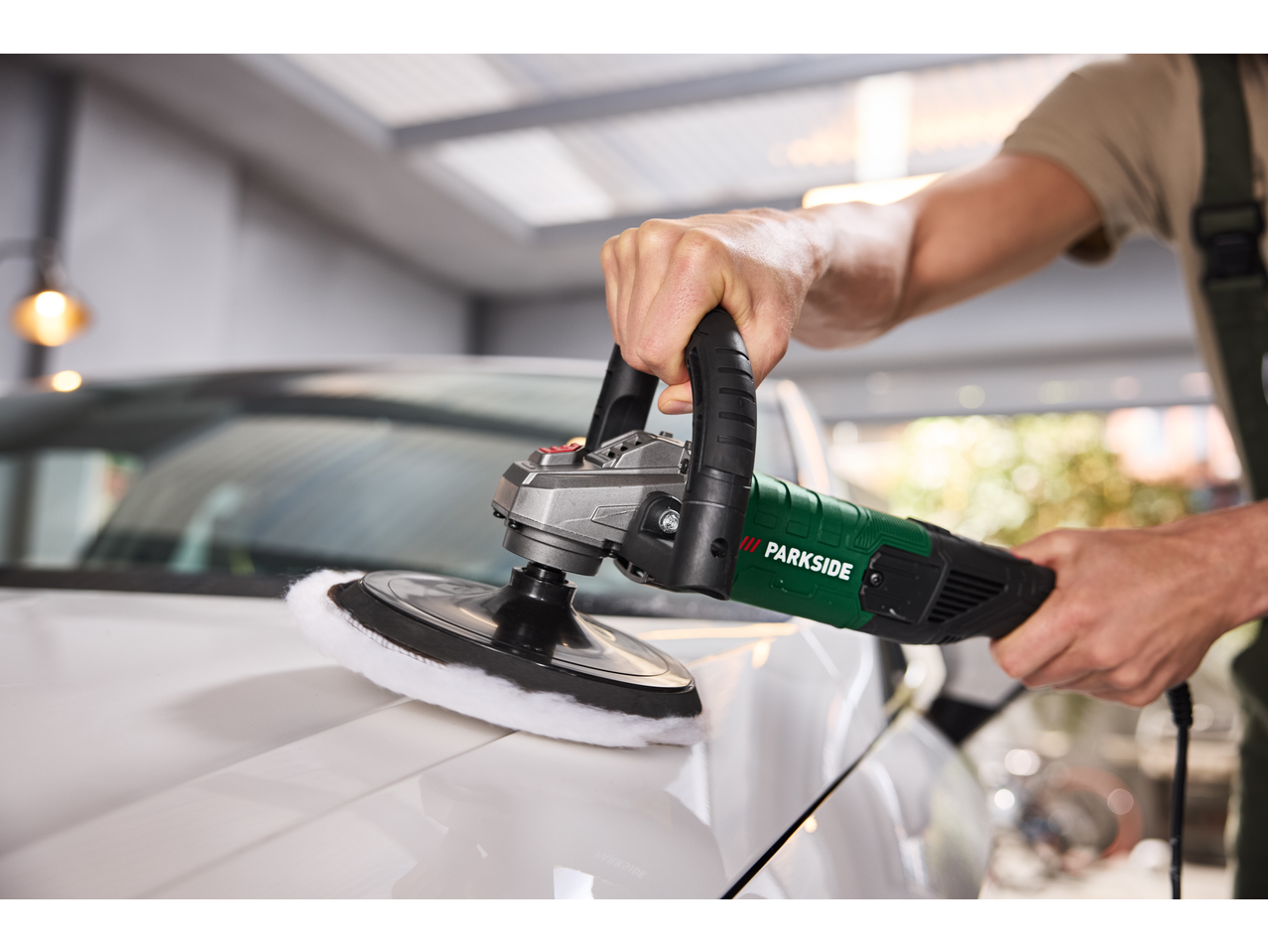 A person polishing a white car with a power polisher.