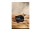 Black air fryer basket on a wooden table with a small bowl and spoon.