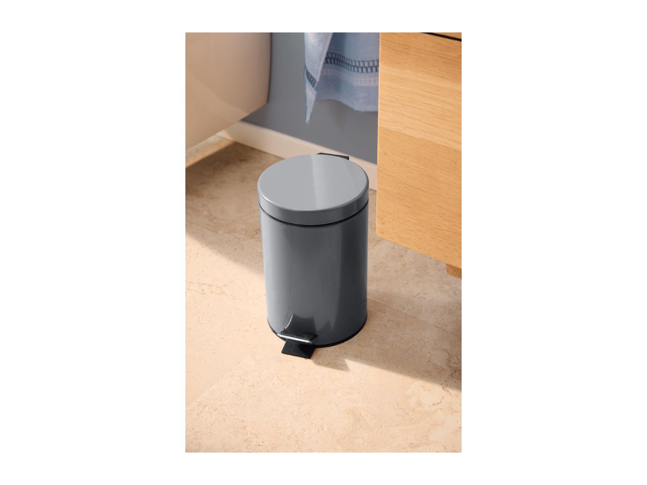 Dark grey pedal bin on a tiled floor in a bathroom setting.