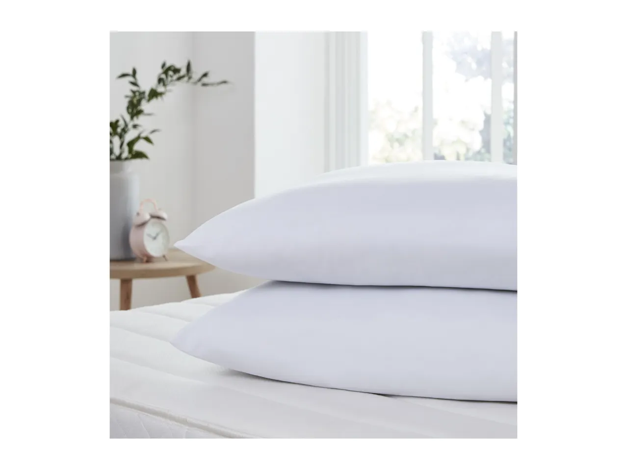 Two white pillows stacked on a mattress in a bright bedroom.