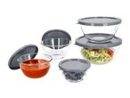 Glass food storage containers with grey lids, some filled with salad, sauce, and olives.