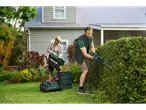 Homem a aparar a sebe, mulher a esvaziar o saco do cortador de relva Parkside® Elektro-Rasenmäher.