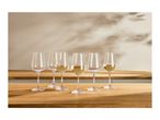 Six wine glasses, some filled with white wine, on a wooden table with shadows.