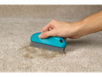 Hand removing pet hair from carpet with blue brush.