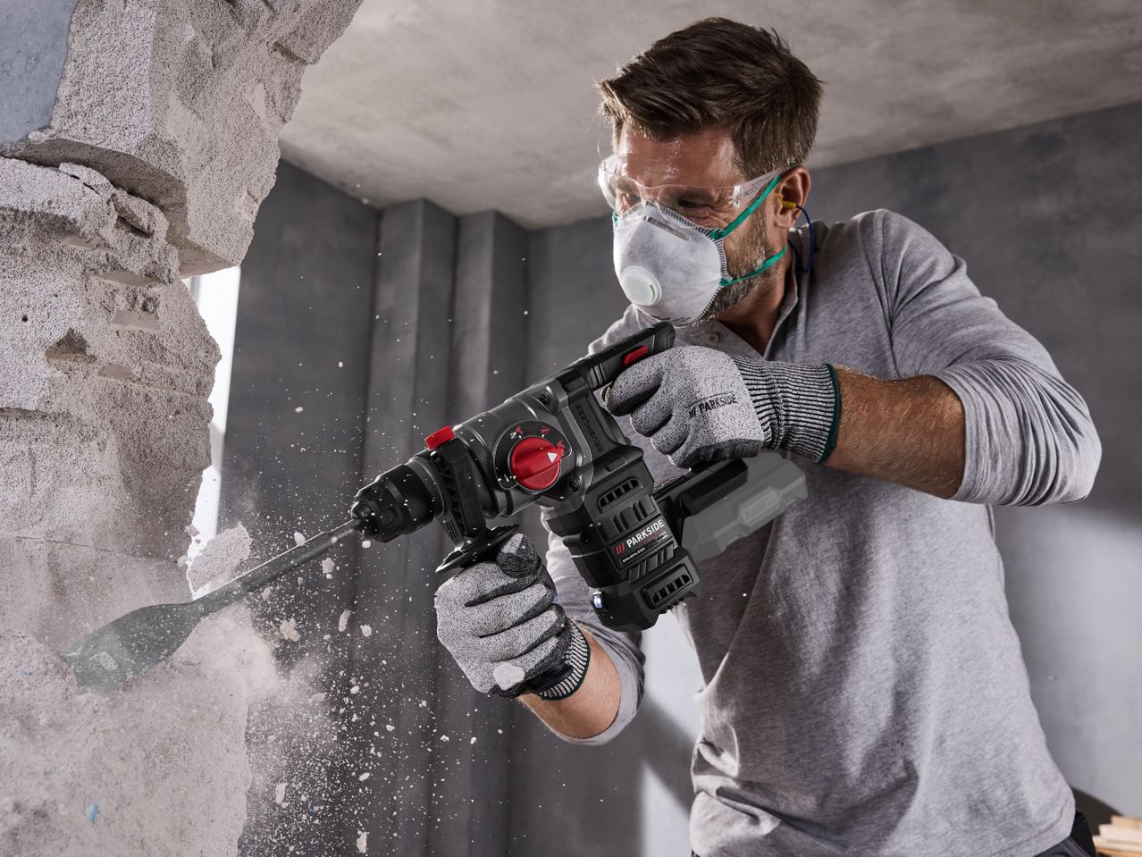 Man in safety gear using a cordless rotary hammer drill to break through a wall.