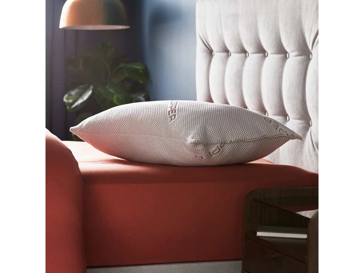 A Codrea pillow rests on a terracotta bedsheet, showcasing its textured fabric and brand logo.