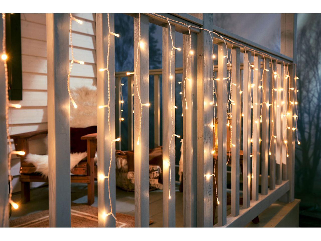 Luci di Natale a cascata su una ringhiera di un portico con sedie e coperte.