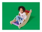 A young child with curly hair sits in a colorful wooden rocking toy, smiling at the camera.