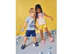 Kids' t-shirts and shorts with a shark and rainbow design, playing with blue balls.