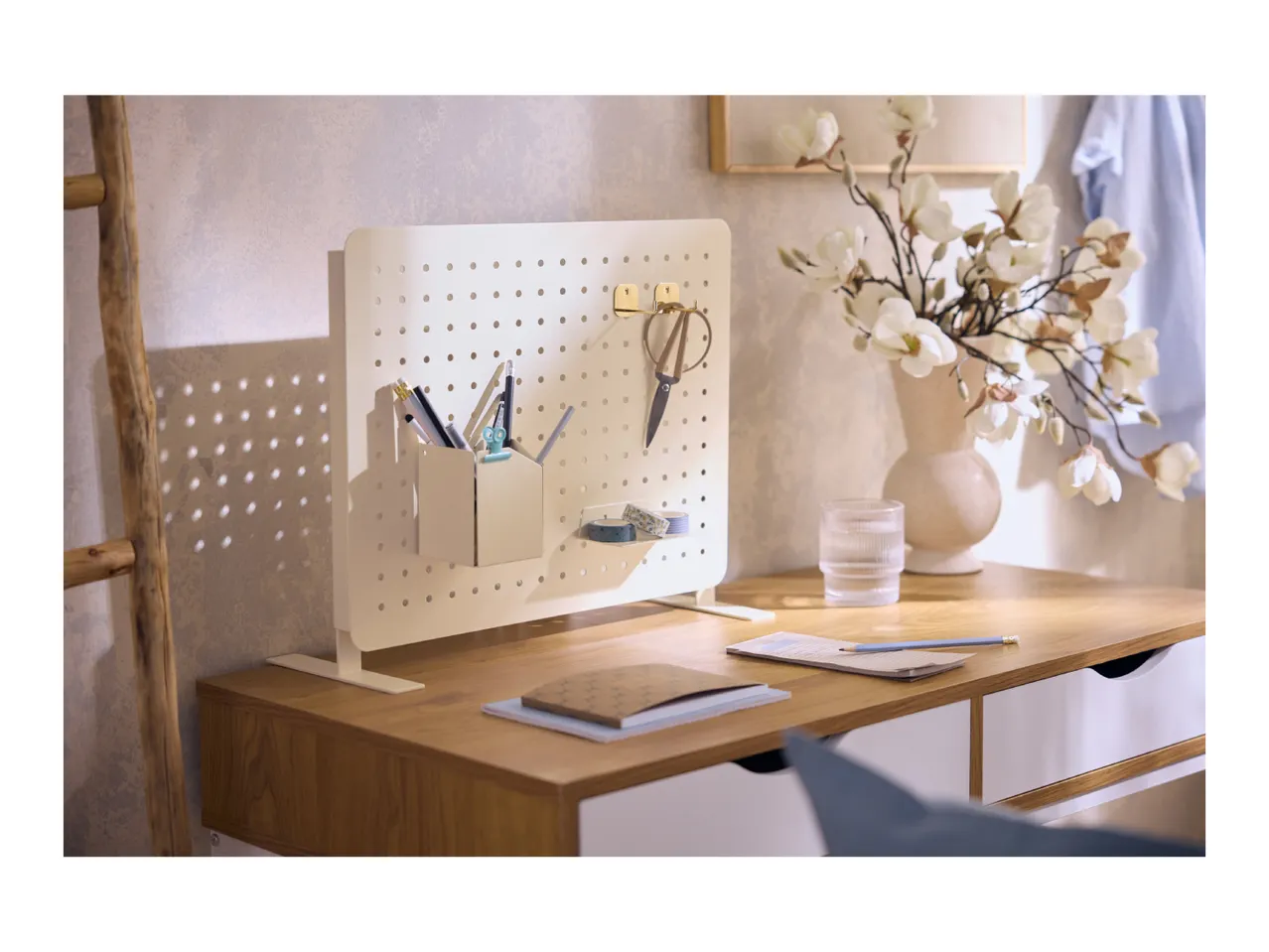 Desk with a white pegboard organizer, pens, scissors, and a vase of flowers.