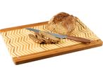 A loaf of multigrain bread, sliced, with a knife on a bamboo cutting board.