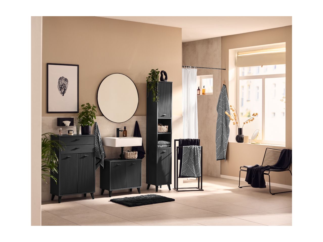 Modern bathroom with black slatted furniture, white sink, round mirror, and patterned towels.