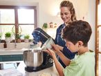 A woman and a boy using a SilverCrest stand mixer in a kitchen.