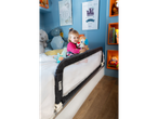 A smiling toddler with a plush toy in a bed with a Safety 1st bed rail.