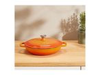 Orange cast iron Dutch oven on a wooden counter with a plant and shadows.