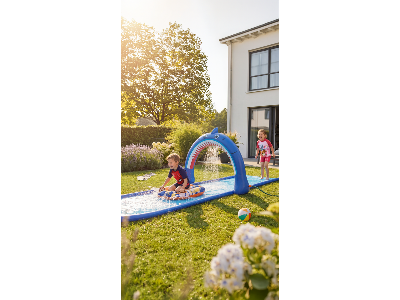 Children playing on a Lupilu water slide with a shark arch in a sunny garden.