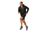 Bărbat alergând purtând o jachetă neagră impermeabilă, pantaloni scurți negri și pantofi sport.