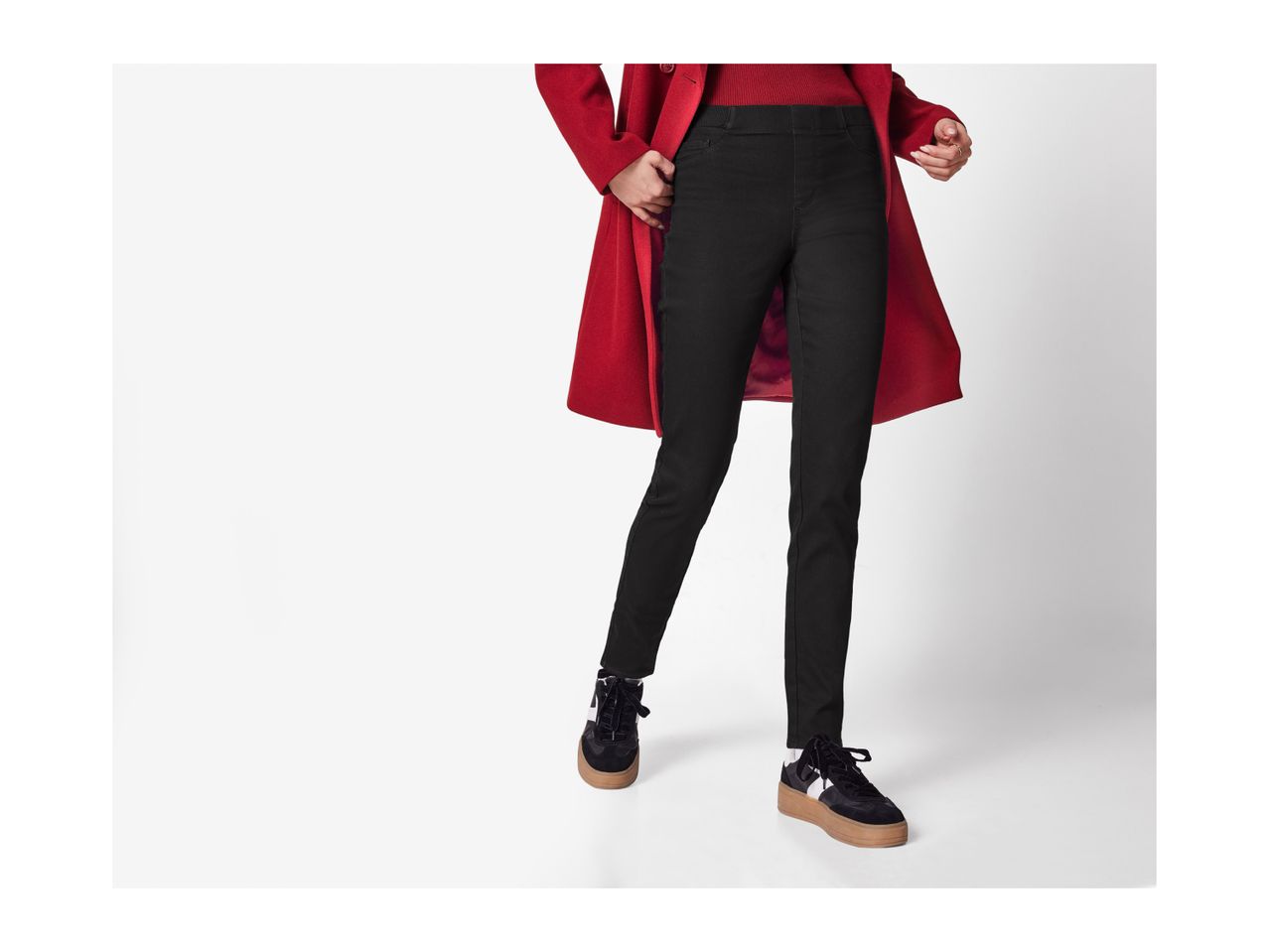 A person wearing a red coat, black pants, and black and white sneakers.